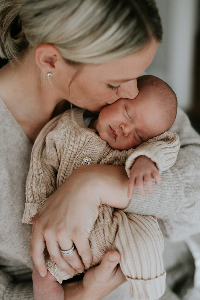 Mother kissing newborn's head while baby sleeps at their newborn session in Melbourne.