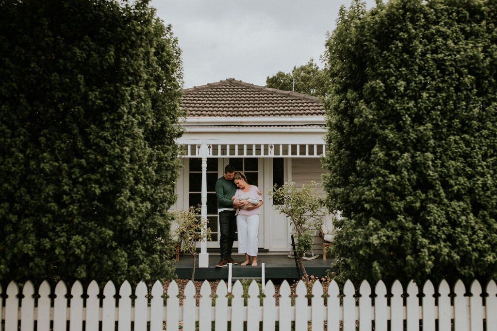 Parents standing outside on the porch holding their newborn baby.