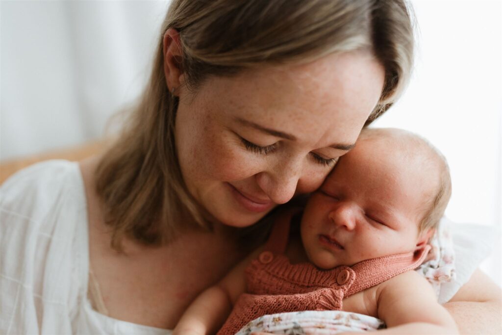 Baby and mother's cheeks touching- both of them with their eyes closed.
