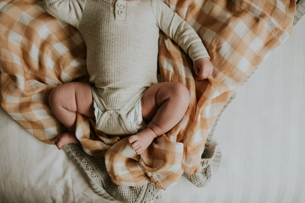Baby lying on yellow muslin wrap with a focus on her little chubby legs.