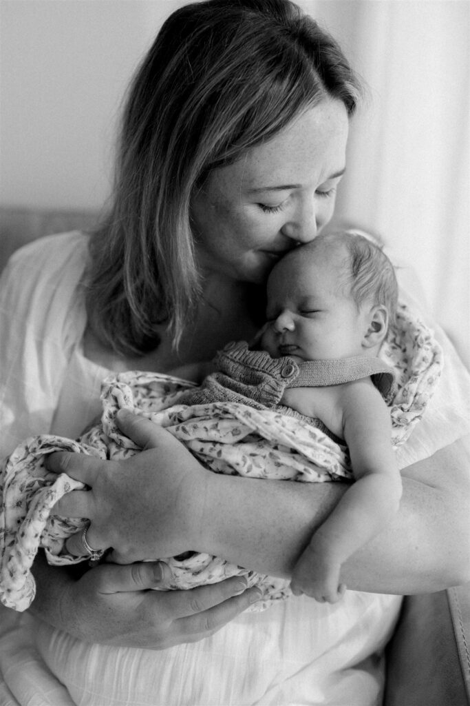 Mother kissing a sleeping baby's head in the soft light.