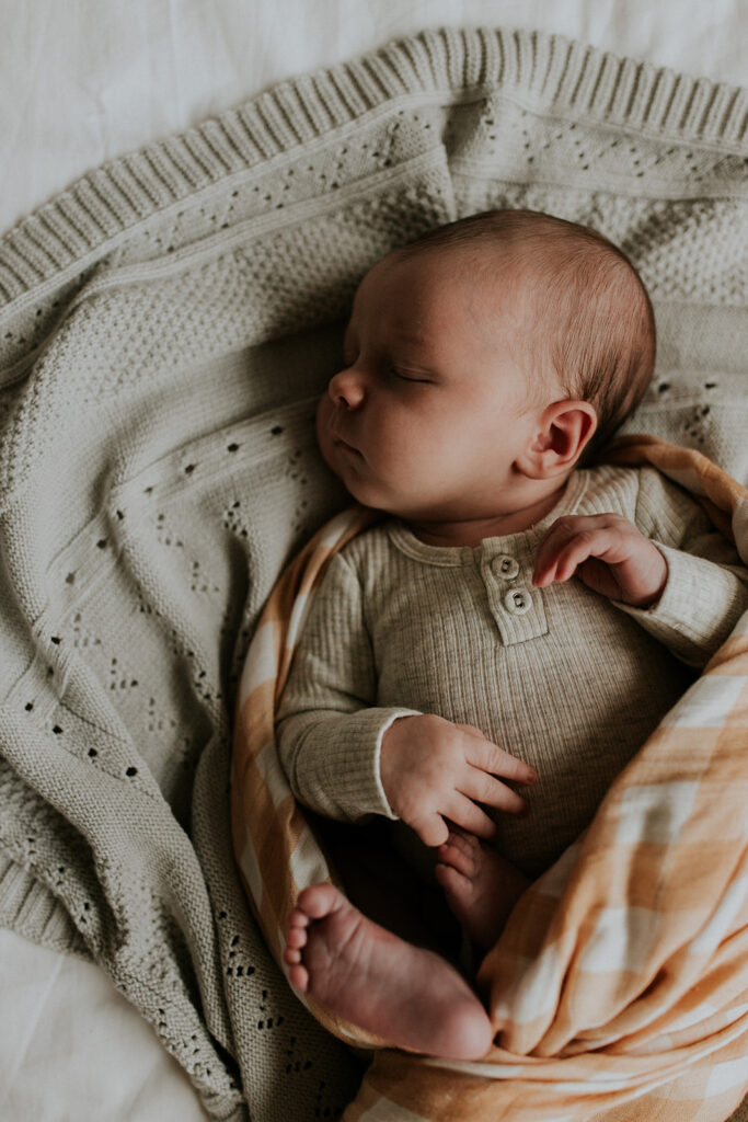 A close up of a newborn baby asleep on the bed, wrapped in a muslin wrap.
