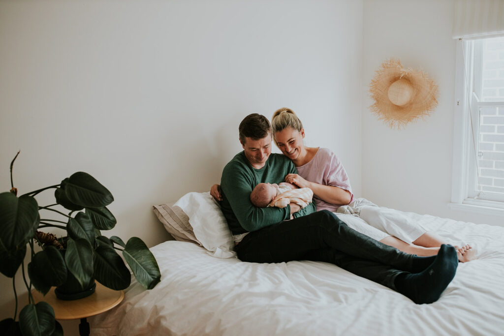Parents sitting on their bed cuddling and laughing at their baby.