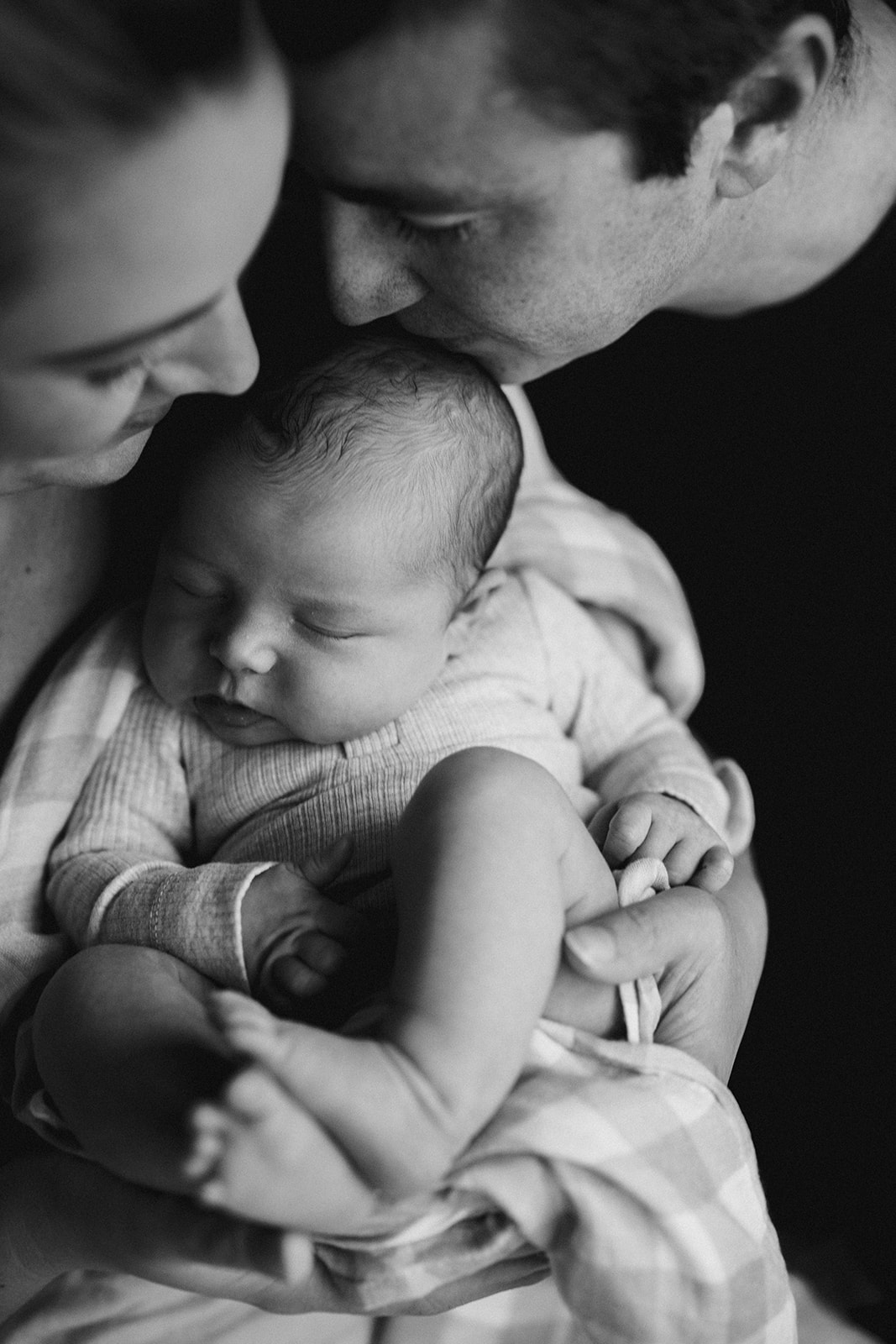 Parents cuddling a newborn baby in the mother's arms.